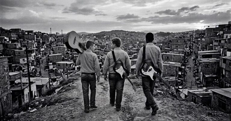 Três adolescentes caminhando por uma comunidade com violão, guitarra e baixo nas costas, a caminho de servir no ministério de louvor